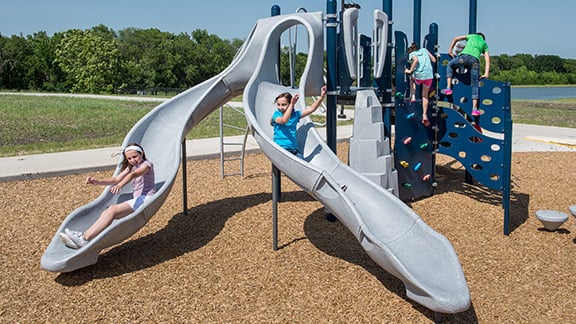 Two children sliding down a double Rushwinder slide, which is a component of a PlayBooster® play structure.