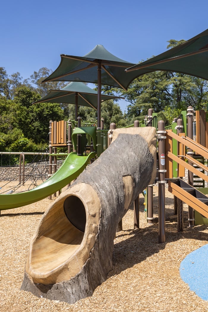 A custom GFRC (glass-fiber-reinforced concrete) playground slide that is designed to appear like a hollow log