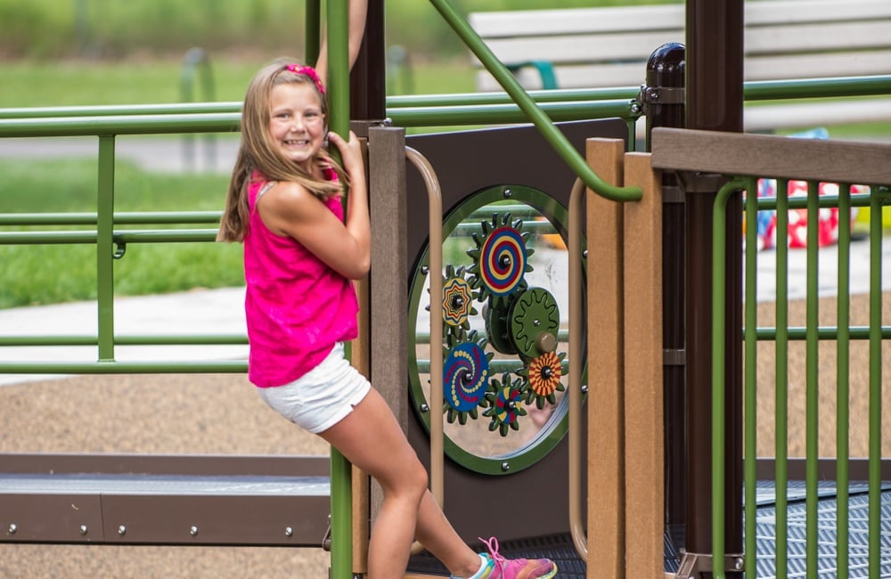 Girl grips a commercial playground firepole that is a component of a larger playground structure