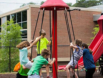 School age boys and girls playing togther on a bright red,rotating spinner, called the TopsyTurny