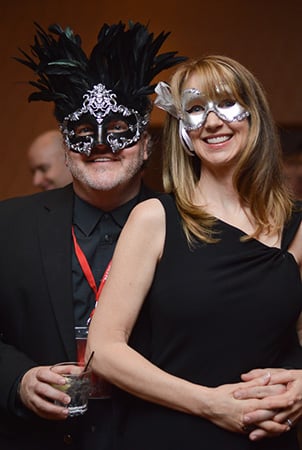 A man and woman smile for the camera while dressed up and wearing masked ball face masks.