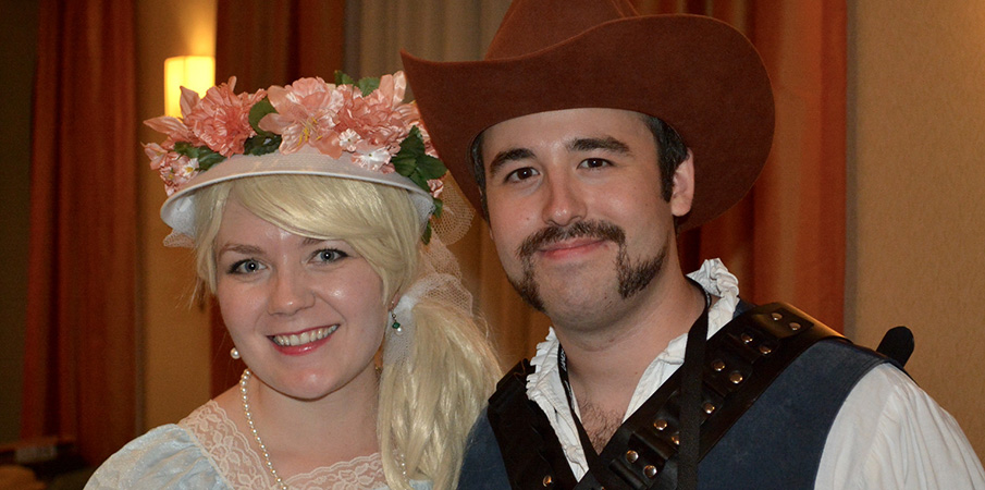 A man and women smile in old western clothing at a holiday party.
