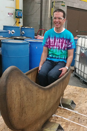 Vice President of sales David Smith smiles while sitting in a glass fiber reinforced concrete canoe in the manufacturing building.