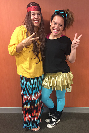 Two women give peace signs to the camera while wearing 70s and 80s on Decades Day.