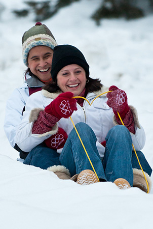 Two people smile as they sled down a snowy hill.