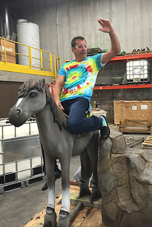 Landscape Structures President Pat Faust pretends to ride a fiber glass reinforced pony concrete statue.