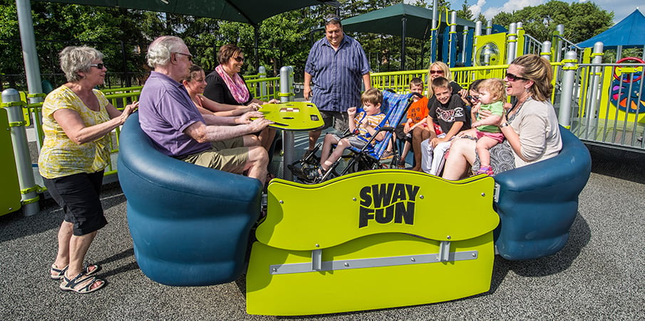 Adults and children all playing on a inclusive Sway Fun glider.