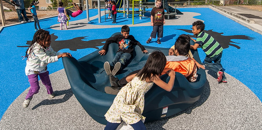 Children play on a inclusive OmniSpin playground spinner. 