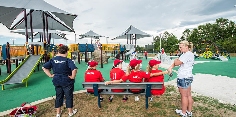 Players and coaches sitting on a bench at a inclusive playground.