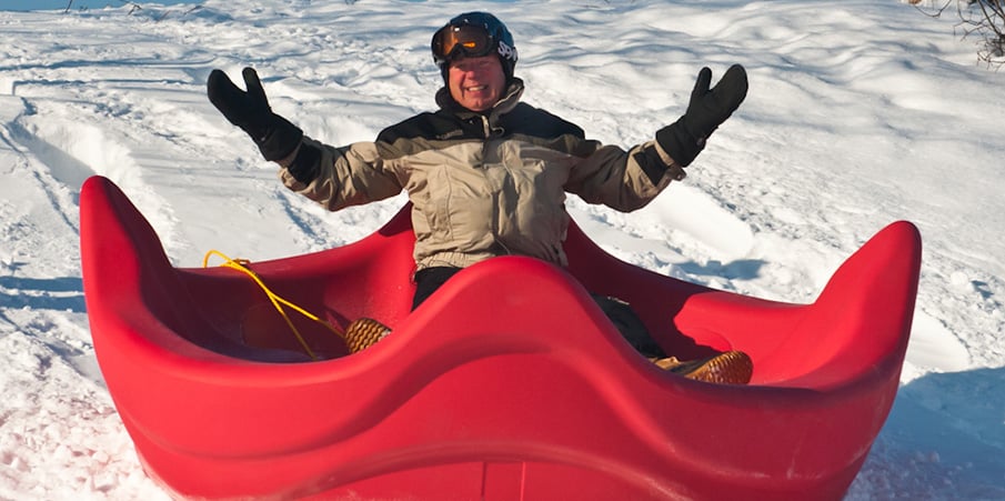 Landscape Structures founder Steve King sliding down a snowy hill on a OmniSpin playground spinner seat.